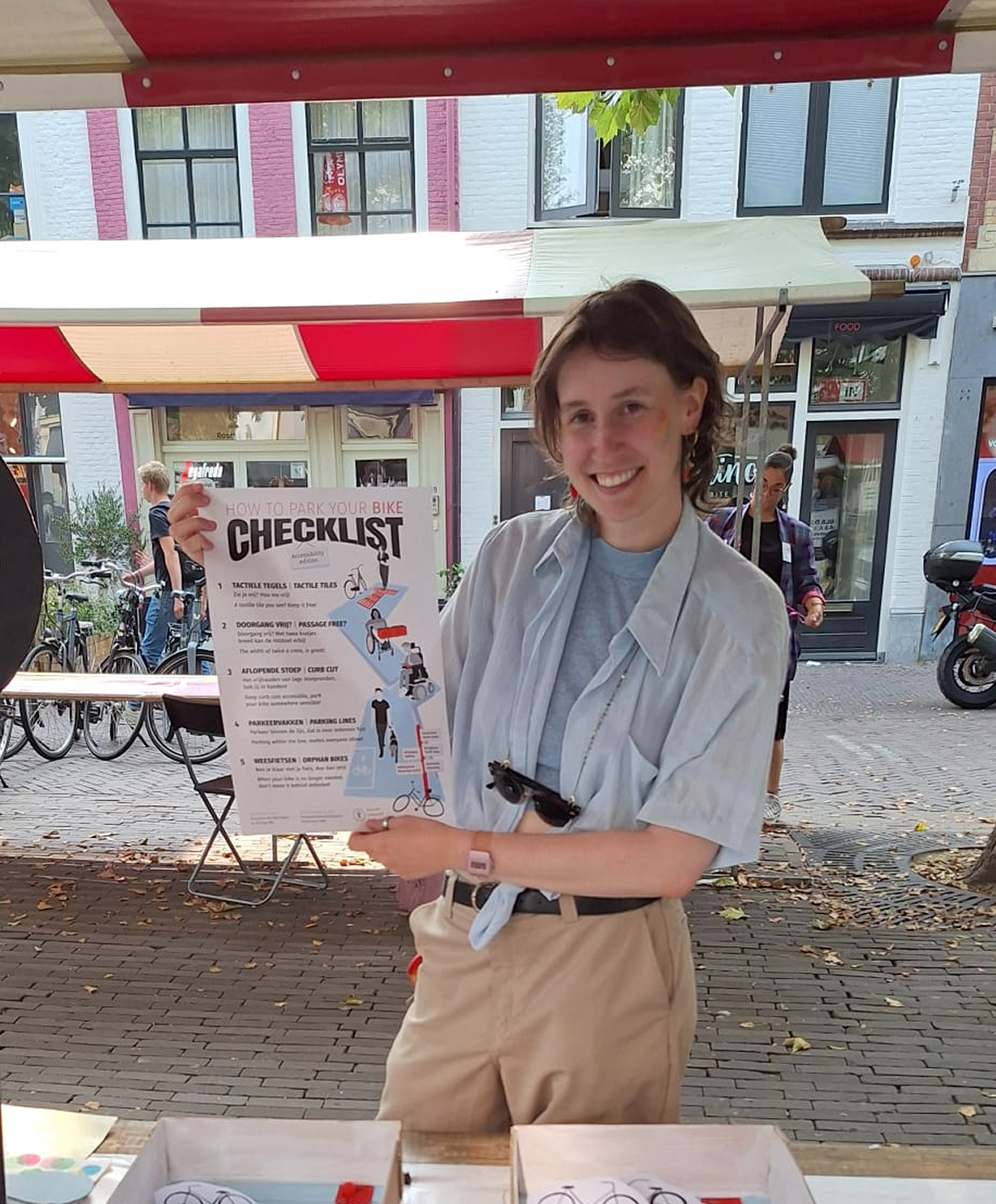 Vrijwilliger toont kranten artikel 'how to park your bike checklist accessiblity edition' bij kraam.