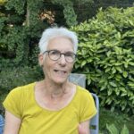 Netty Jongepier, Secretaris Inclusie Collectief Delft, een oudere vrouw met bril en geel shirt buiten in groen decor.