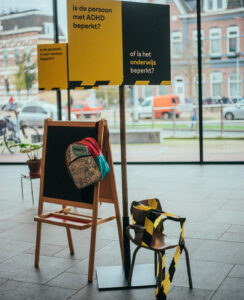Binnenruimte met schildersezel en geel informatiebord bij raam.