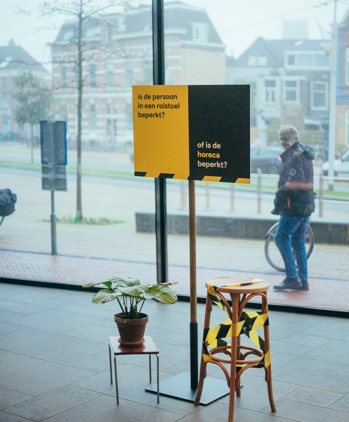 Binnenruimte met grote ramen, gele borden en bezoekers buiten zichtbaar.